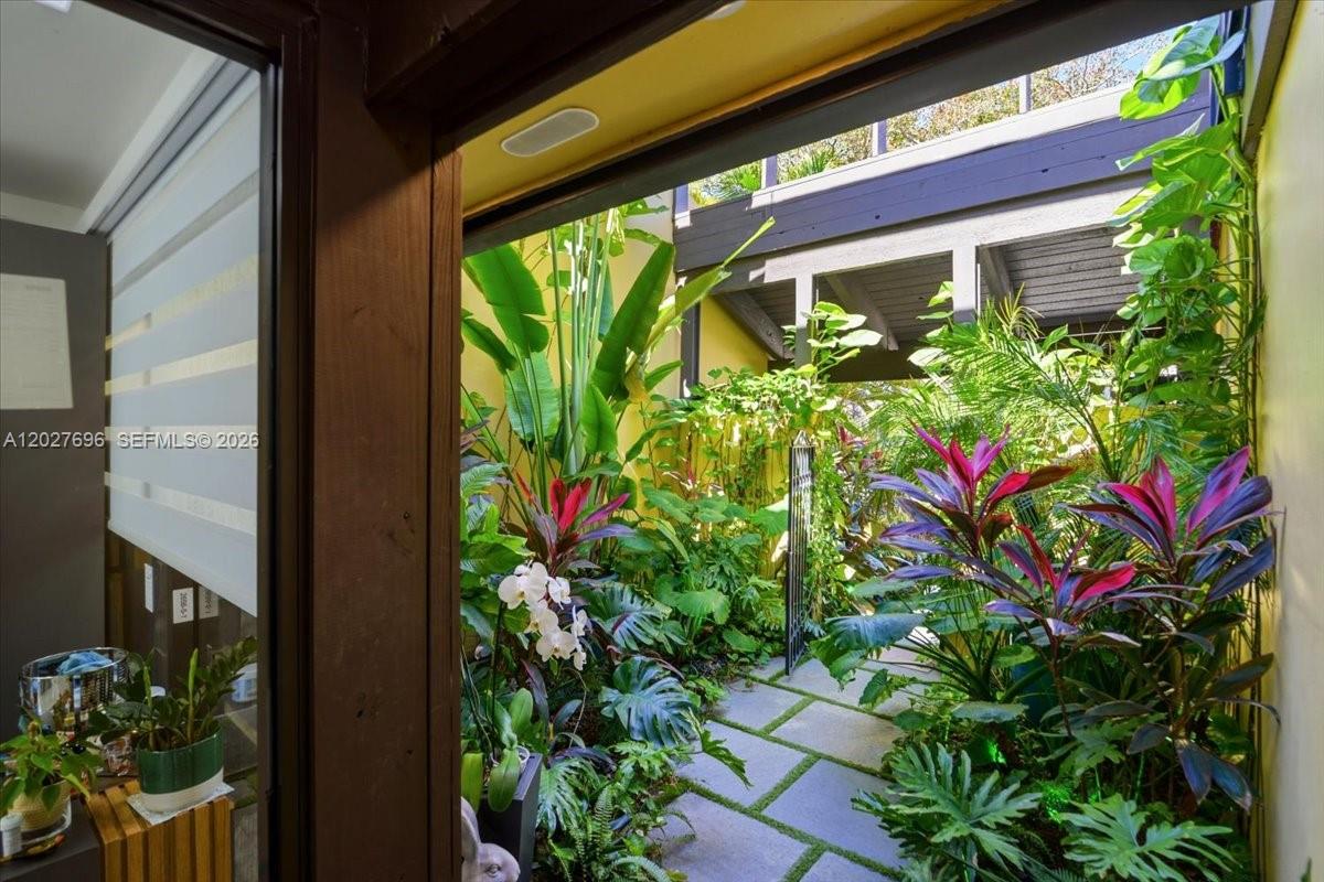 A view from an interior doorway looks out onto a lush, stone-paved garden courtyard — 3629 Estepona Ave # 27, Doral FL 33178, DORAL, FL