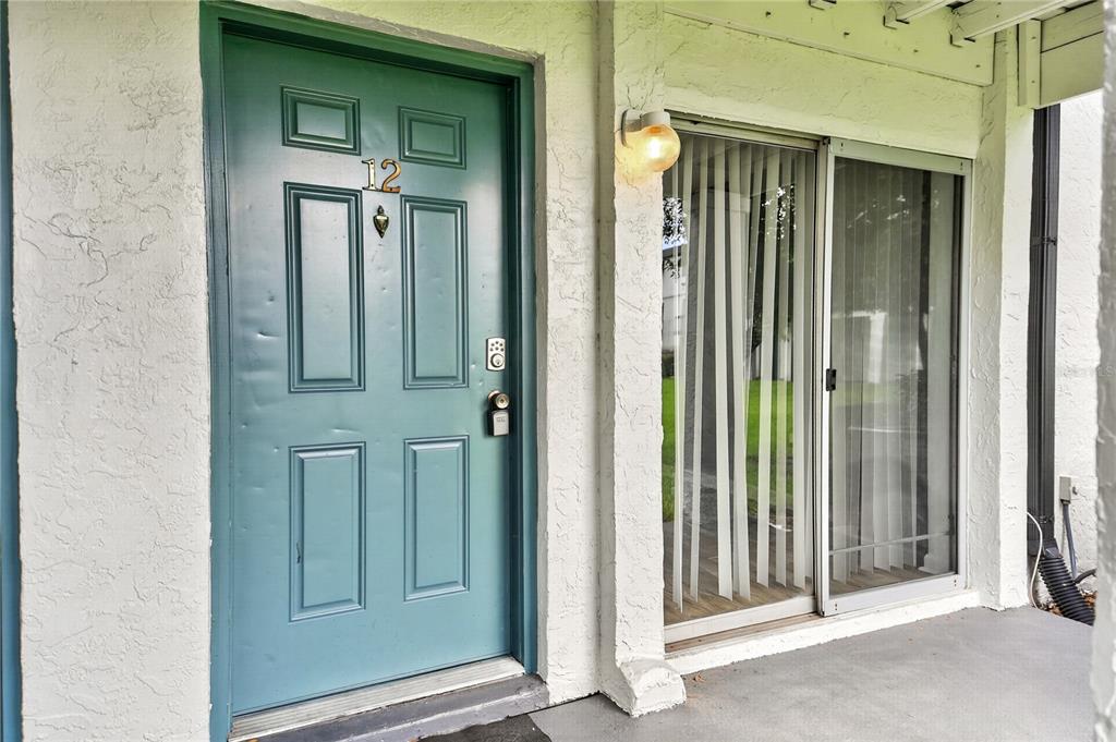 A teal front door with the number 12 and a sliding glass door on a porch — 4203 S. SEMORAN BLVD UNIT 12, ORLANDO, FL