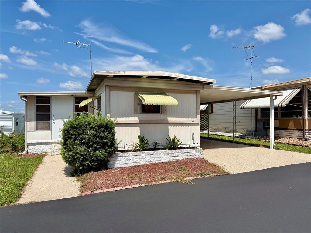 A single-story mobile home with a white exterior, green window awnings, and a paved driveway — 7103 EL MEYERS STREET, ZEPHYRHILLS, FL