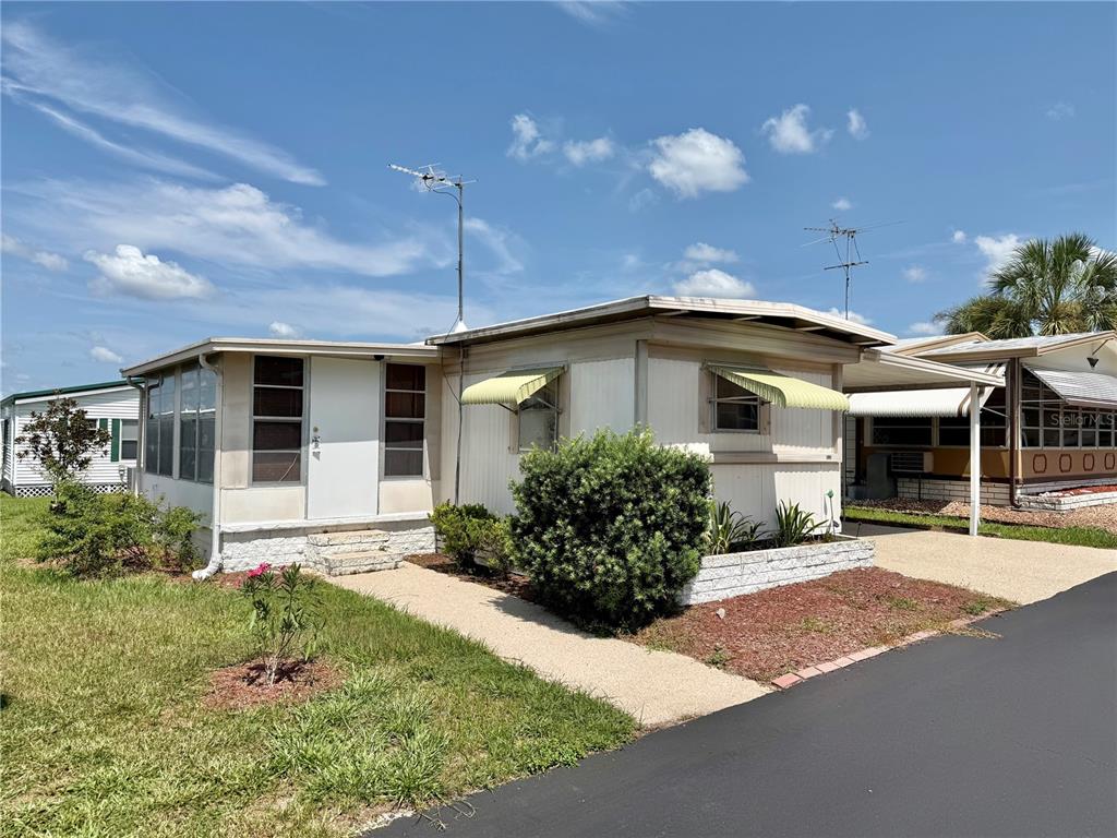 A single-story mobile home features a side carport and a small front garden area — 7103 EL MEYERS STREET, ZEPHYRHILLS, FL