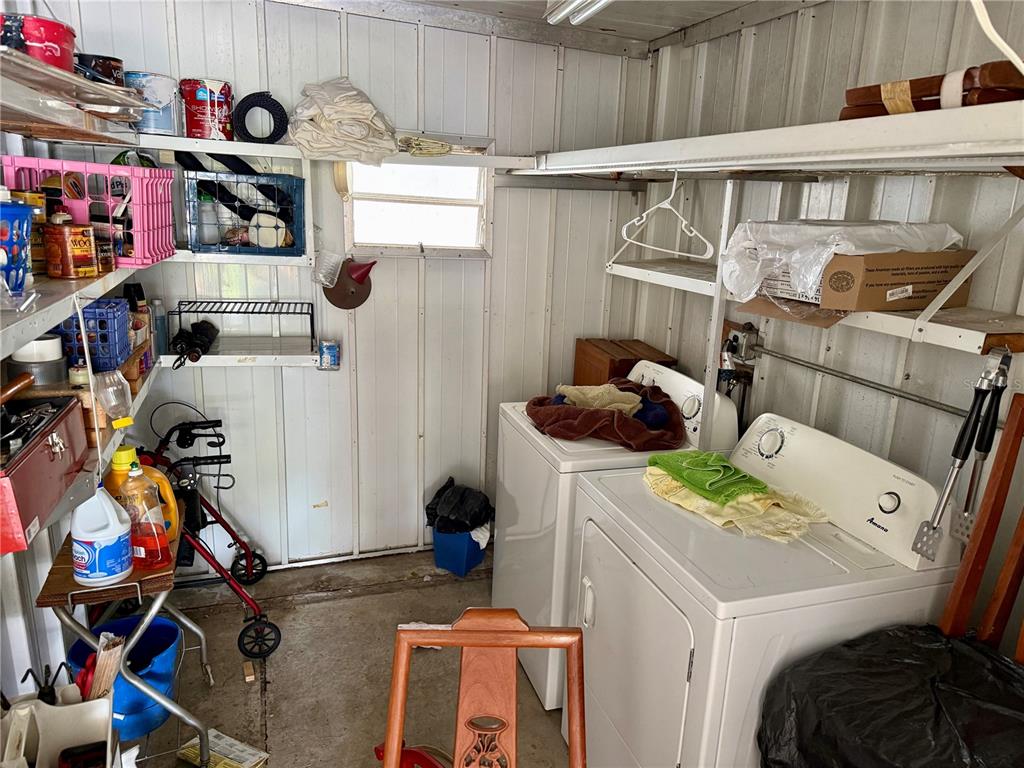 A utility room features a white washer and dryer, metal shelving, and various storage items — 7103 EL MEYERS STREET, ZEPHYRHILLS, FL