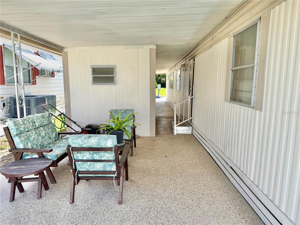 A covered patio with outdoor furniture, a small plant, and a walkway leading to a door — 7103 EL MEYERS STREET, ZEPHYRHILLS, FL