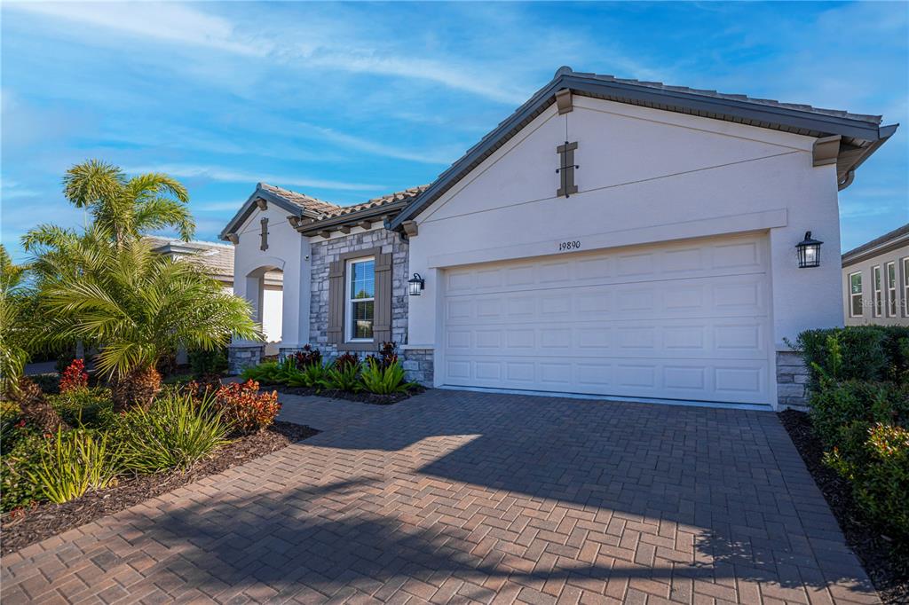 The exterior of a house features a paved driveway, a two-car garage, and stone accents — 19890 MONTENERO WAY, VENICE, FL