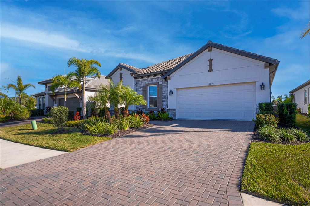 A single-story house with a white stucco facade, stone accents, and a brick paver driveway — 19890 MONTENERO WAY, VENICE, FL