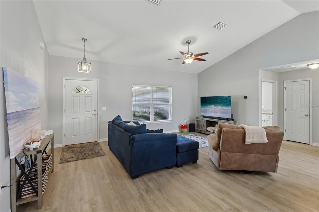 A living room features light wood-look flooring, a blue sectional sofa, and a brown armchair — 9170 SE 150TH STREET, SUMMERFIELD, FL