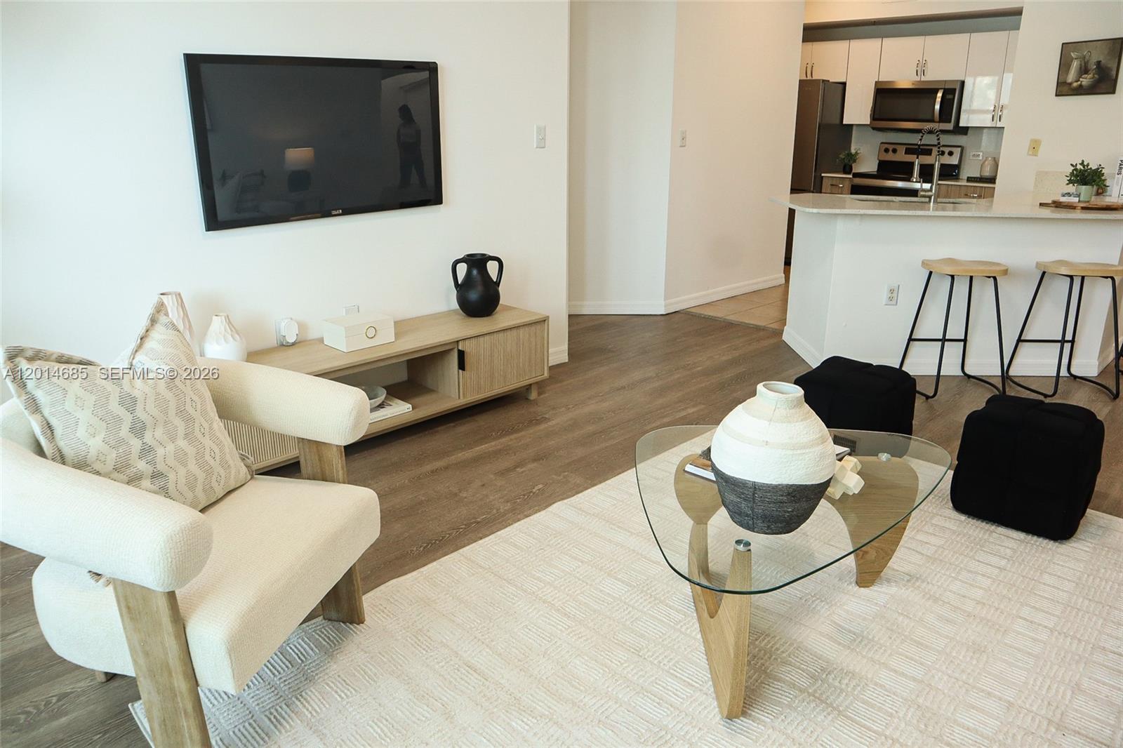 A living room features a white armchair, a glass coffee table, and an open kitchen — 9172 Collins Ave # 212, Surfside FL 33154, SURFSIDE, FL