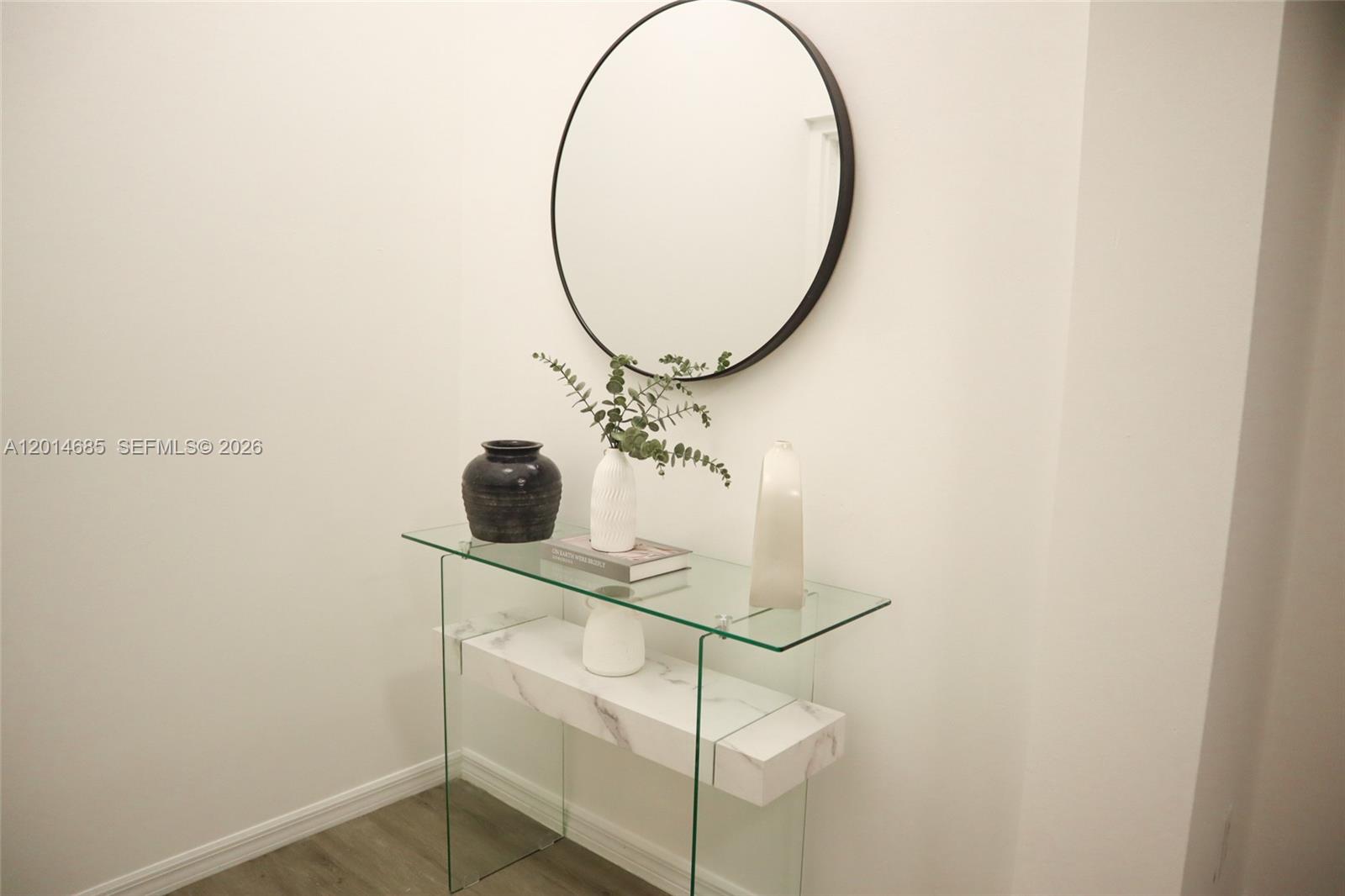 A glass console table with a marble shelf sits against a wall below a mirror — 9172 Collins Ave # 212, Surfside FL 33154, SURFSIDE, FL