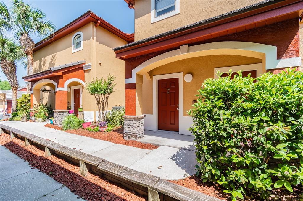 A view of two tan townhome entrances with red doors, stone pillars, and a wooden border — 2265 PORTOFINO PLACE UNIT 21-212, PALM HARBOR, FL