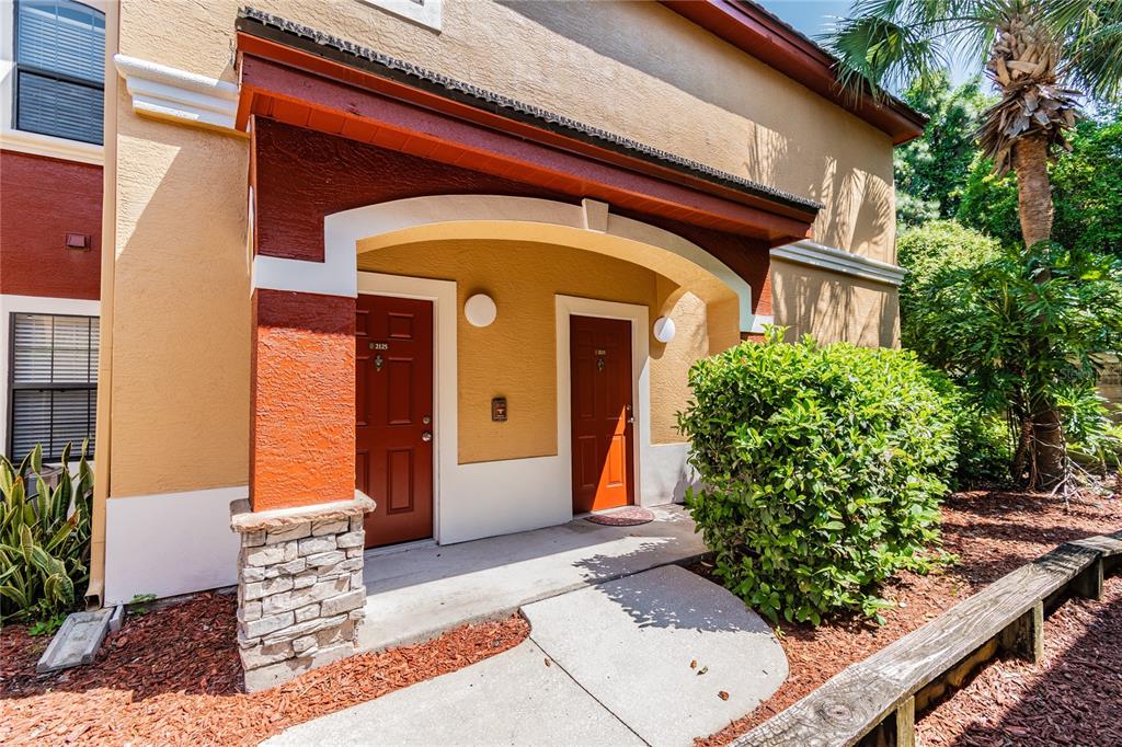 An exterior view of a building entrance with two red doors under a covered porch — 2265 PORTOFINO PLACE UNIT 21-212, PALM HARBOR, FL