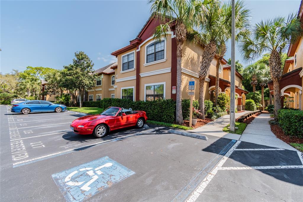 A red convertible is parked in a handicap space in front of a tan apartment building — 2265 PORTOFINO PLACE UNIT 21-212, PALM HARBOR, FL
