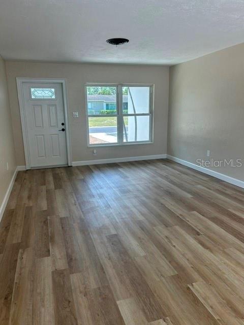 An empty room features light wood-look flooring, a white front door, and a large window — 3066 66TH WAY N, ST PETERSBURG, FL