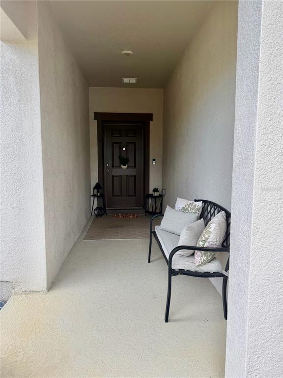 A covered entryway features a dark brown front door, a metal bench, and light-colored walls — 1817 SUNDANCE CHASE ROAD, MINNEOLA, FL