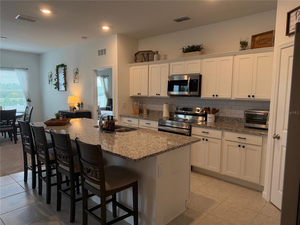 A kitchen features white cabinets, granite countertops, a large island with bar stools, and appliances — 1817 SUNDANCE CHASE ROAD, MINNEOLA, FL