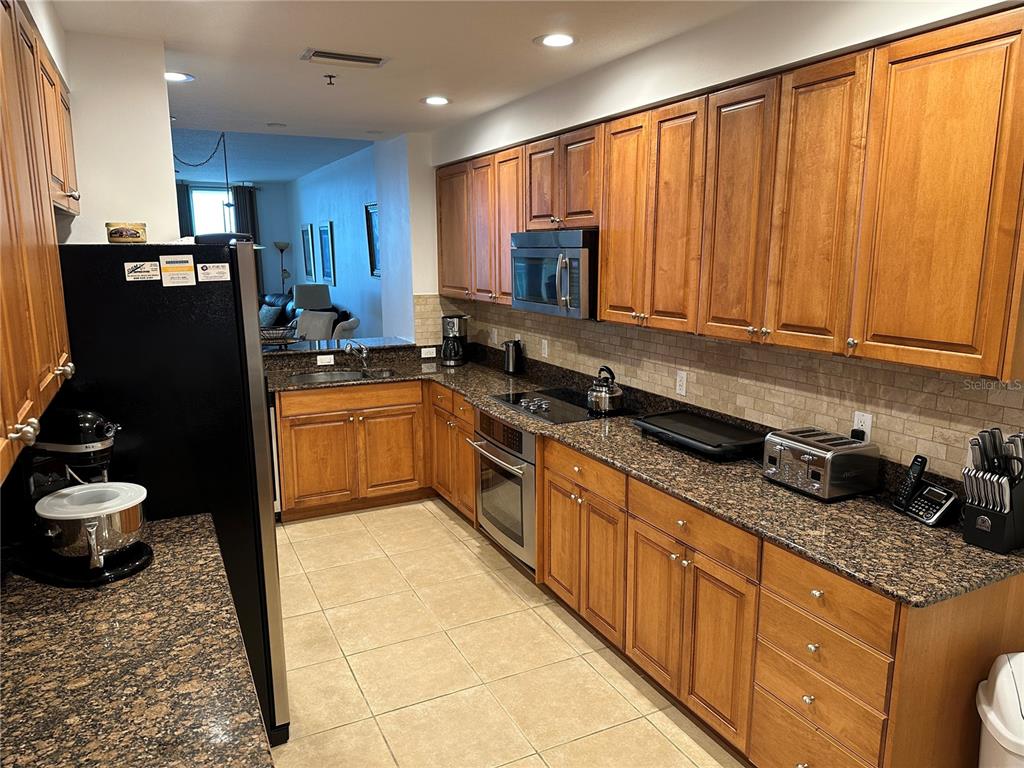 A kitchen features wood cabinets, granite countertops, stainless steel appliances, and beige tile flooring — 615 RIVIERA DUNES WAY UNIT 406, PALMETTO, FL