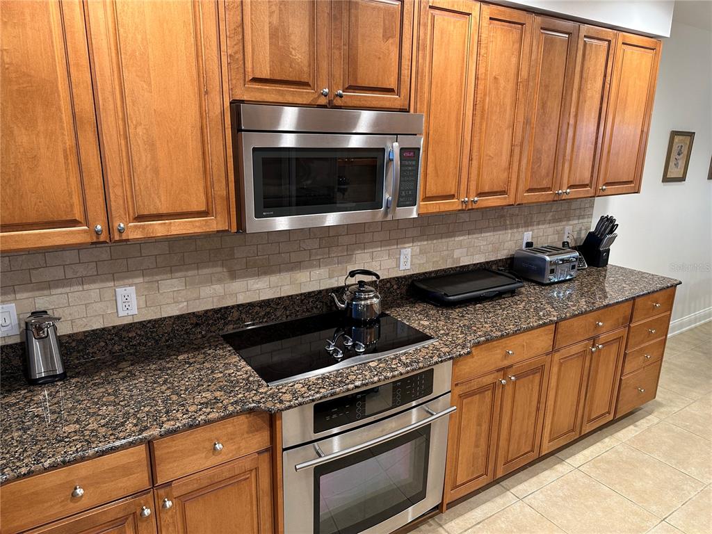 A kitchen features wood cabinets, granite countertops, a stainless steel oven, and a microwave — 615 RIVIERA DUNES WAY UNIT 406, PALMETTO, FL
