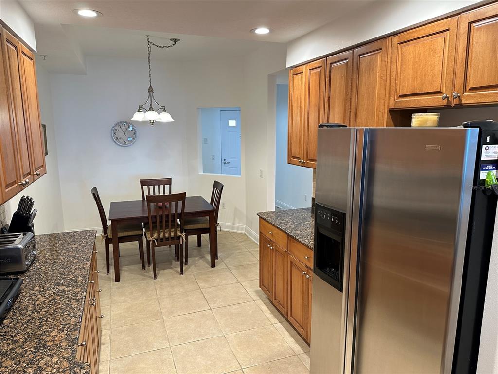 A kitchen with wood cabinets, granite countertops, and a dining area with a table — 615 RIVIERA DUNES WAY UNIT 406, PALMETTO, FL