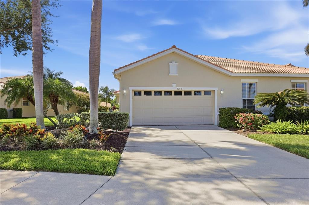 A beige single-story house features a two-car garage, a concrete driveway, and palm trees — 8050 VICTORIA FALLS CIRCLE, SARASOTA, FL