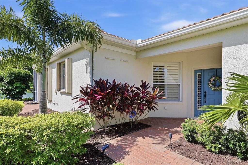 A brick walkway leads to the blue front door of a house with stucco siding — 8050 VICTORIA FALLS CIRCLE, SARASOTA, FL