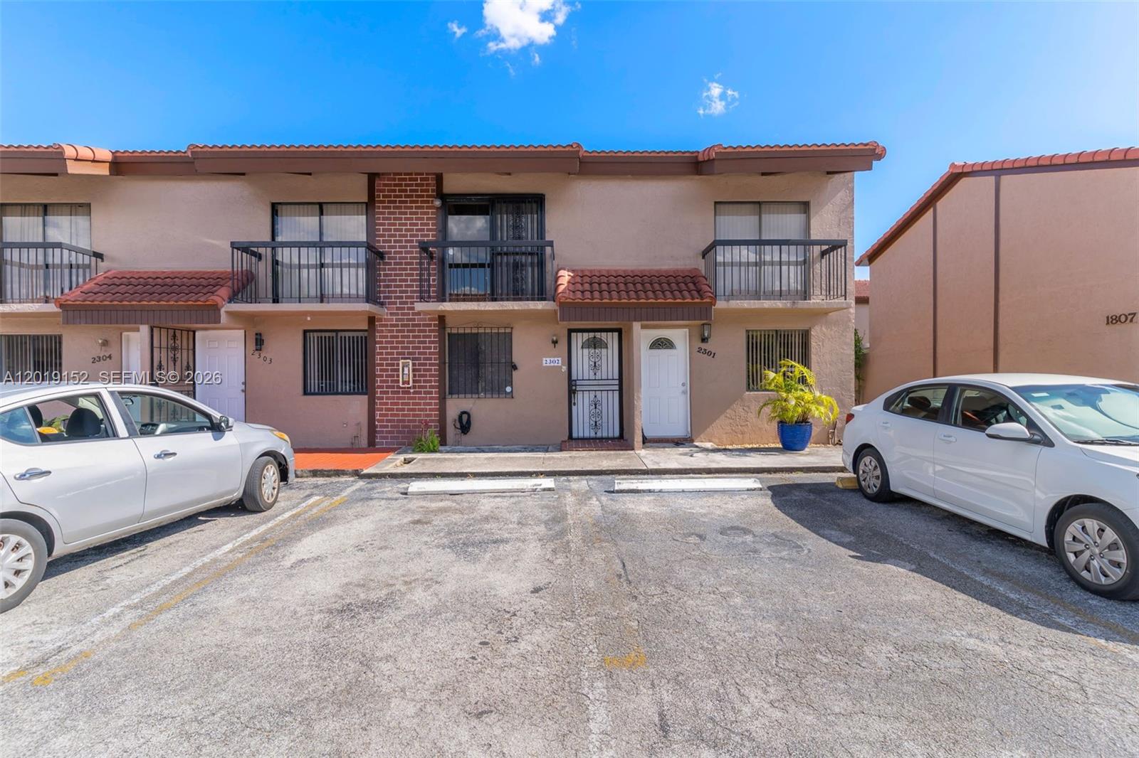 A two-story townhouse exterior features a tan stucco facade, balconies, and a paved parking area — 1811 SW 107th Ave # 2302, Miami FL 33165, MIAMI, FL