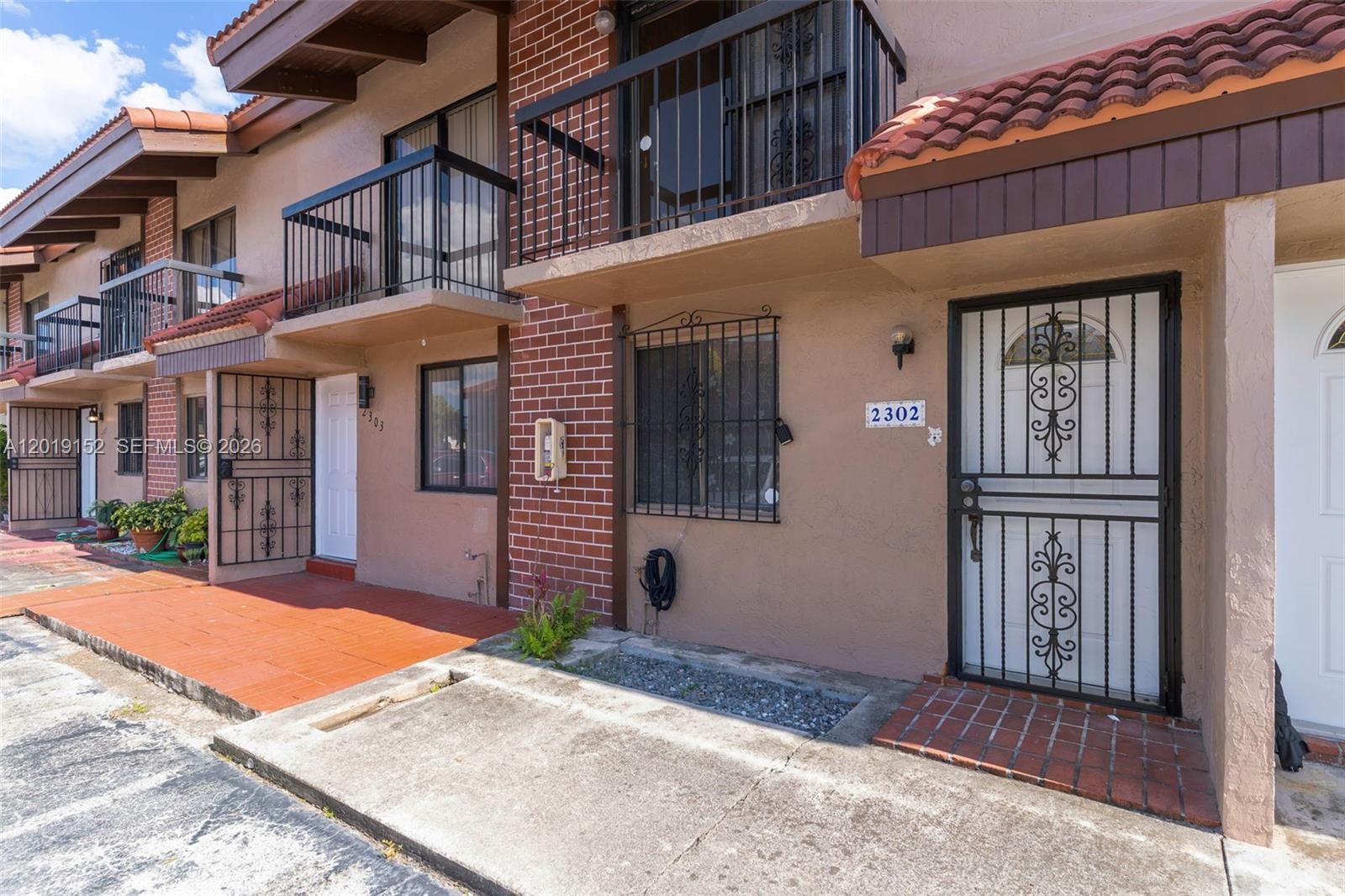 An exterior view of a two-story townhouse complex with brick accents and metal security doors — 1811 SW 107th Ave # 2302, Miami FL 33165, MIAMI, FL