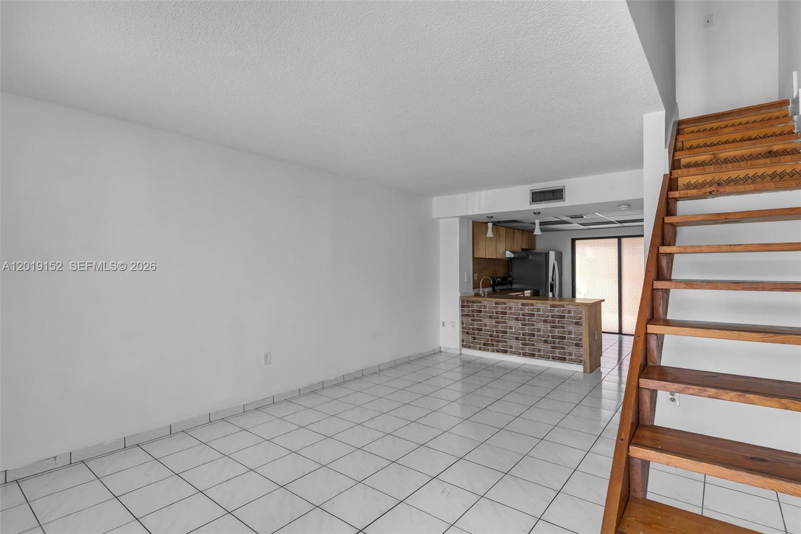 An open living area features white tile floors, a brick-faced kitchen counter, and wooden stairs — 1811 SW 107th Ave # 2302, Miami FL 33165, MIAMI, FL