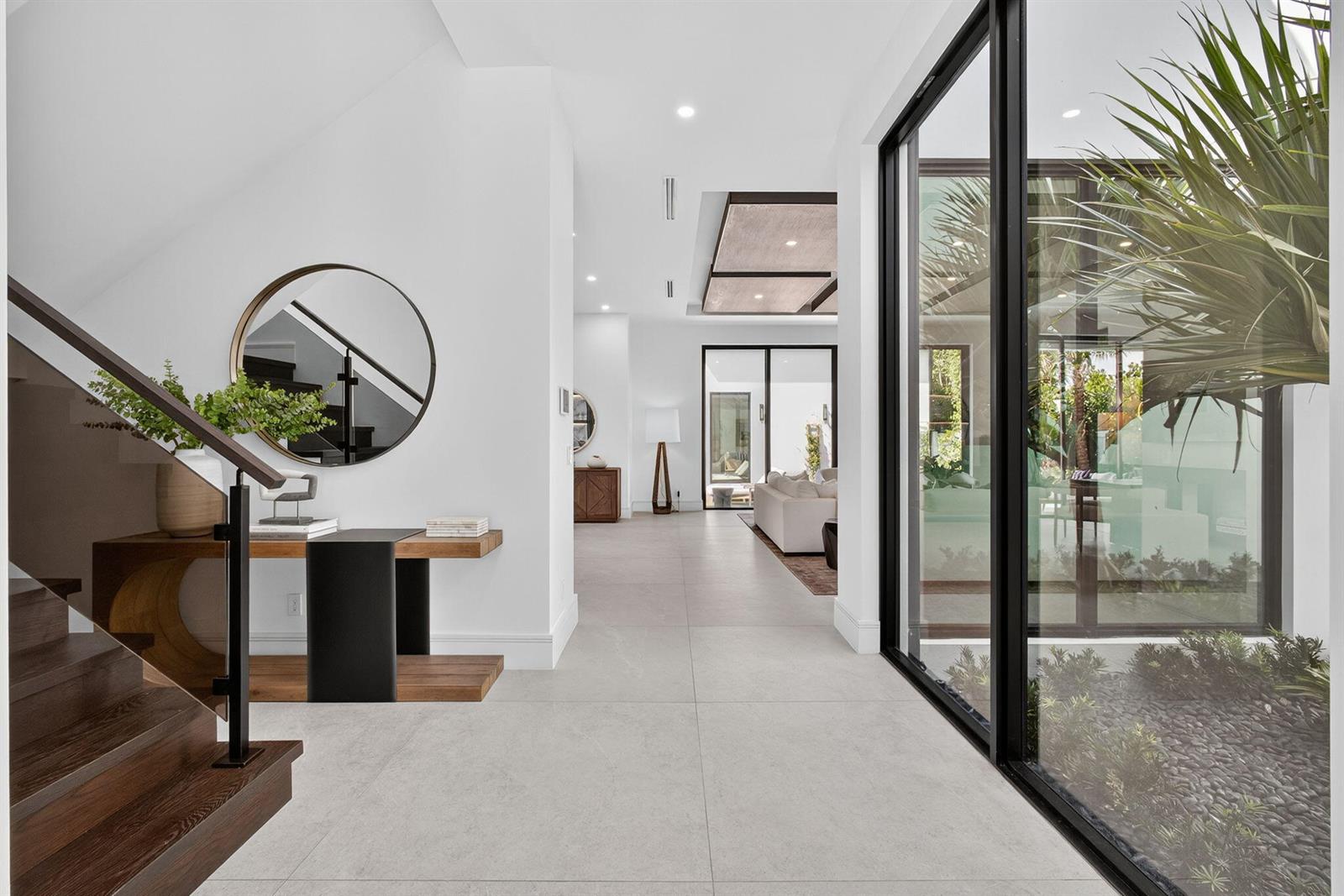 A modern entryway features a wooden staircase, a round mirror, and a glass-walled interior courtyard — 123 Murray Road, West Palm Beach FL 33405, WEST PALM BEACH, FL