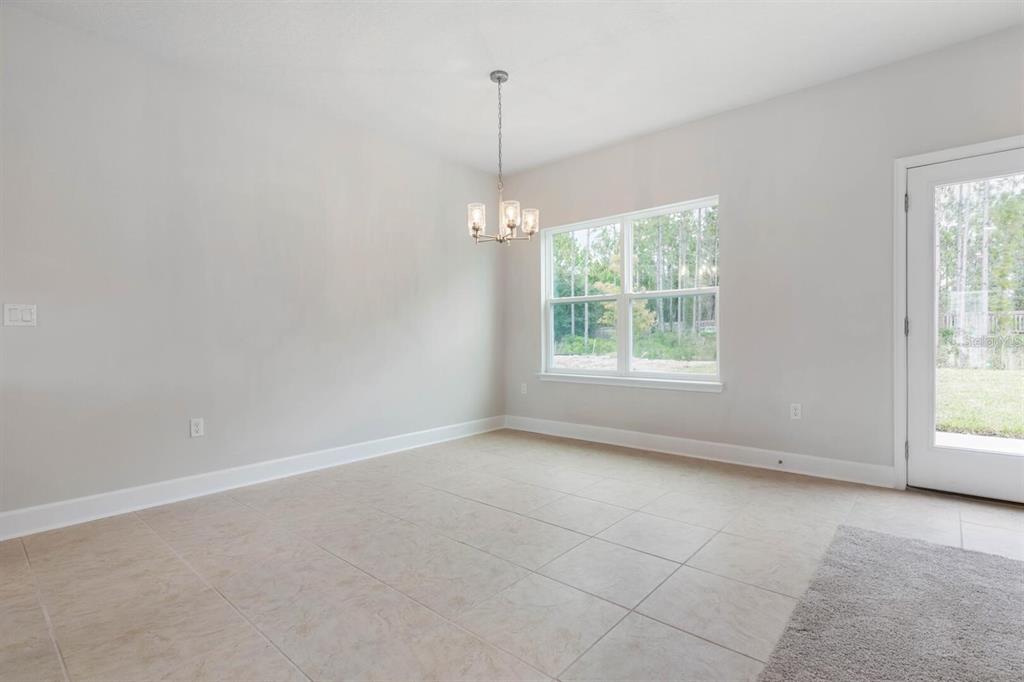 An empty dining room features tile flooring, a chandelier, a large window, and a glass door — 24 RALE PLACE, PALM COAST, FL