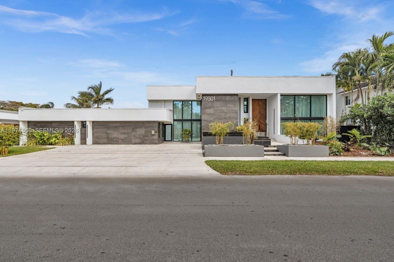 A modern, single-story house with a flat roof, large windows, and a concrete driveway — 19801 NE 23rd Ave, Miami FL 33180, MIAMI, FL