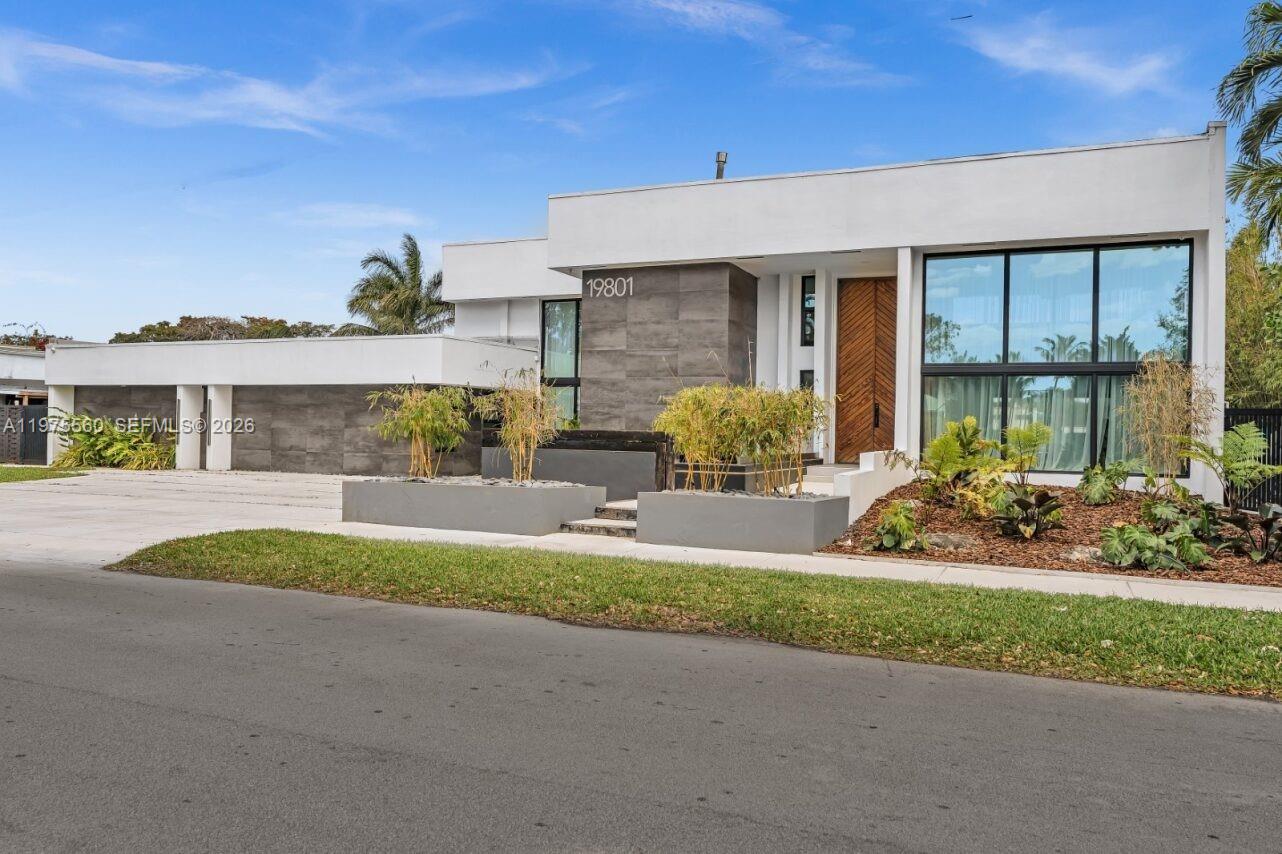 A modern, flat-roofed house features white walls, dark stone accents, and large glass windows — 19801 NE 23rd Ave, Miami FL 33180, MIAMI, FL
