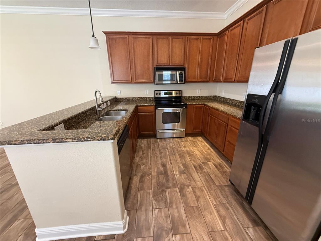 A kitchen features wood cabinets, granite countertops, stainless steel appliances, and wood-look tile flooring — 2618 E CENTRAL BOULEVARD, ORLANDO, FL