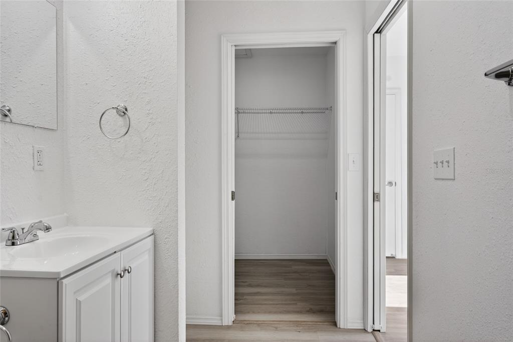 A bathroom vanity with a white sink sits beside a walk-in closet with shelving — 536 ROYAL PALM DRIVE, KISSIMMEE, FL