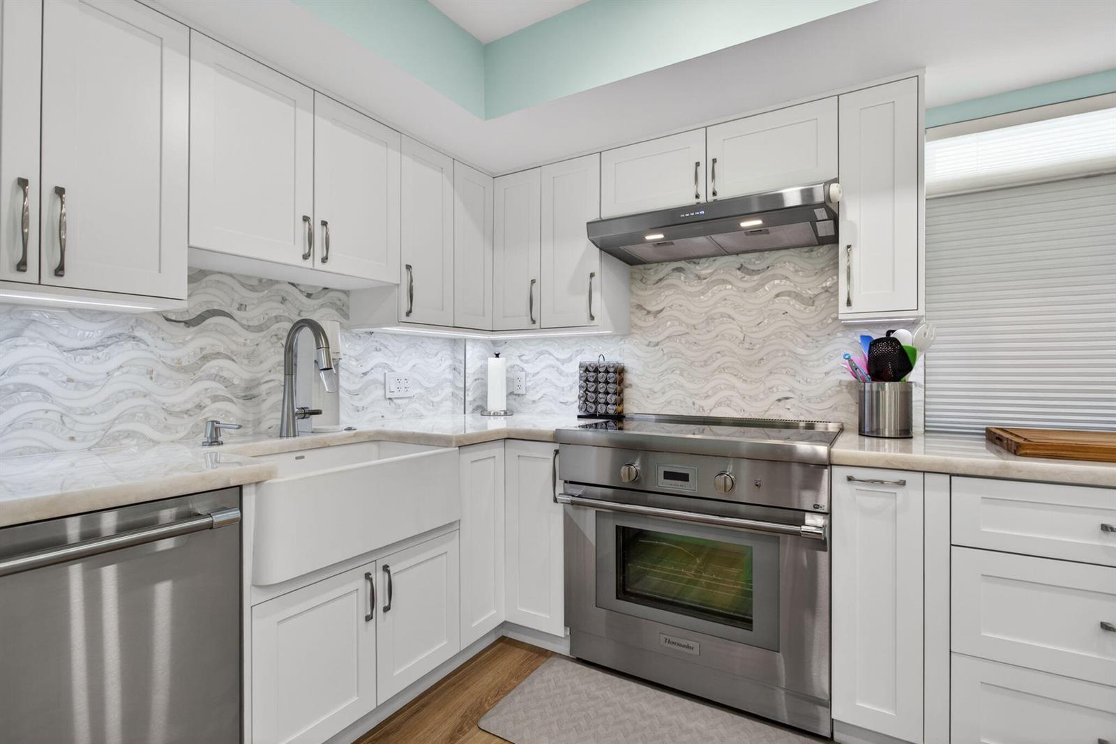 A kitchen features white cabinets, a farmhouse sink, stainless steel appliances, and wavy tile backsplash — 3100 NE 48th Court # 214, Lighthouse Point FL 33064, LIGHTHOUSE POINT, FL