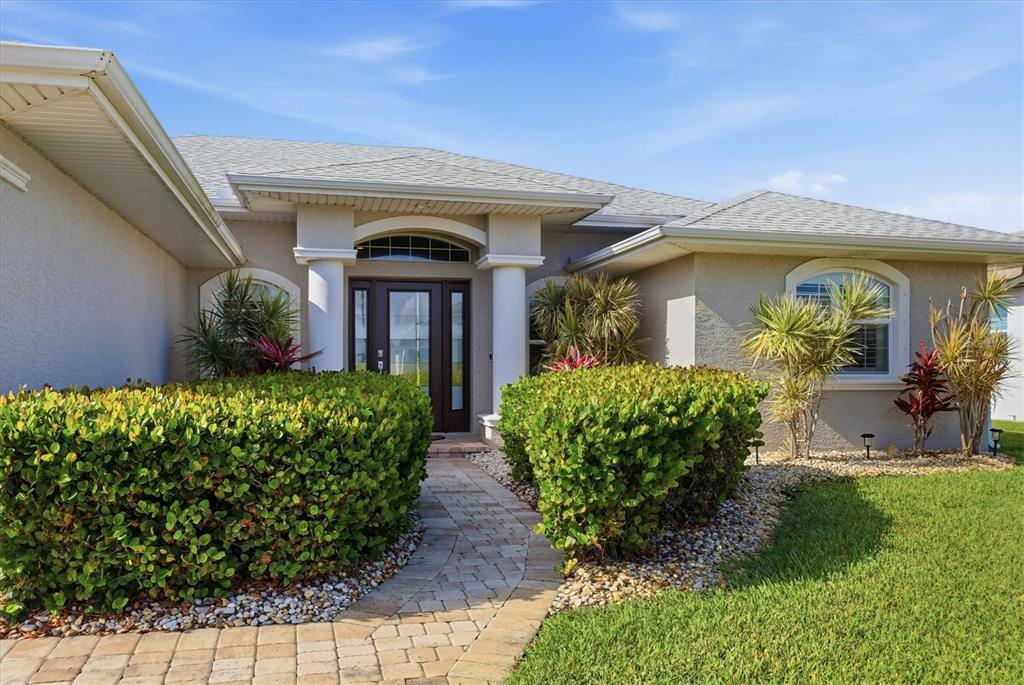 A beige house exterior features a stone walkway leading to a front door with columns — 15738 APPLEWHITE CIRCLE, PORT CHARLOTTE, FL