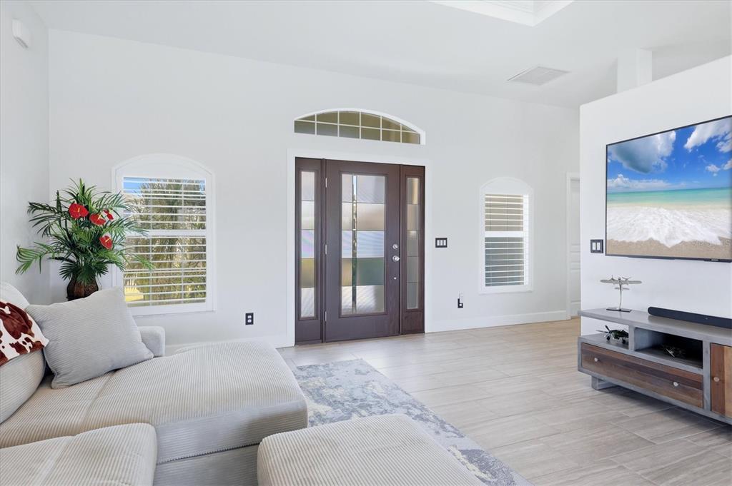 A living room features light tile floors, a sectional sofa, and a dark wood front door — 15738 APPLEWHITE CIRCLE, PORT CHARLOTTE, FL