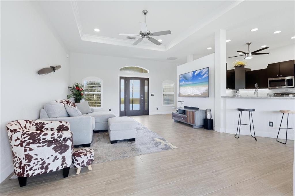 A living room with light tile floors, a cow-print chair, and an open kitchen area — 15738 APPLEWHITE CIRCLE, PORT CHARLOTTE, FL
