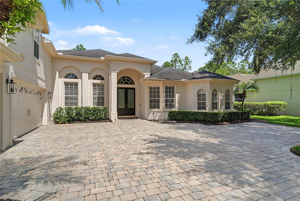 A beige single-story house with a paved driveway, arched windows, and a dark front door — 2710 REGAL PINE TRAIL, OVIEDO, FL