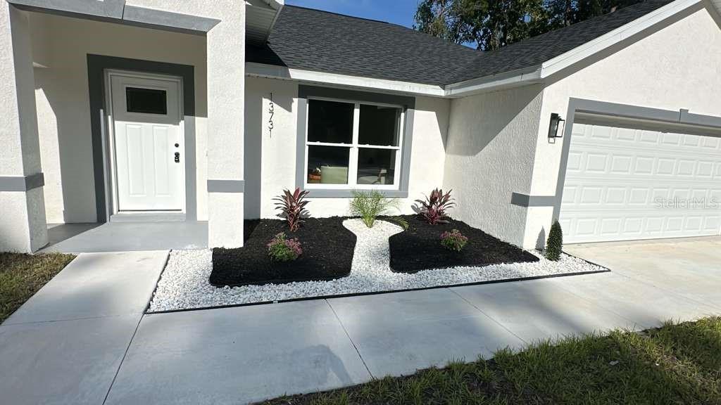 The exterior of a house features a white front door, a garage, and landscaped beds — 13731 SW 89TH CIRCLE, OCALA, FL