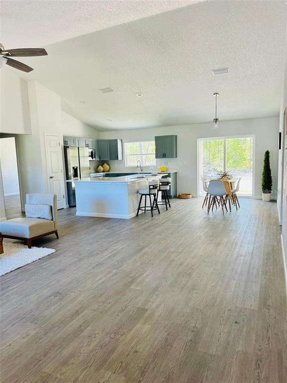 An open-concept kitchen features a large island, gray cabinetry, and light wood-look flooring — 13731 SW 89TH CIRCLE, OCALA, FL