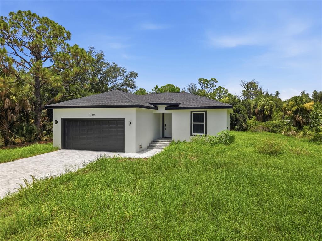 A single-story white house with a dark garage door sits on a grassy lot — 17180 DRAYTON LANE, PORT CHARLOTTE, FL