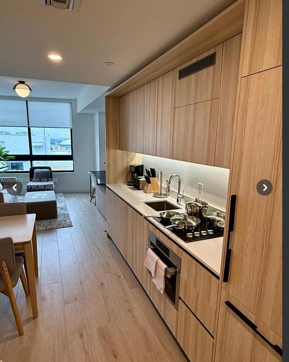A modern kitchen features light wood cabinetry, white countertops, and stainless steel appliances — 225 N Miami Ave # 212, Miami FL 33128, MIAMI, FL