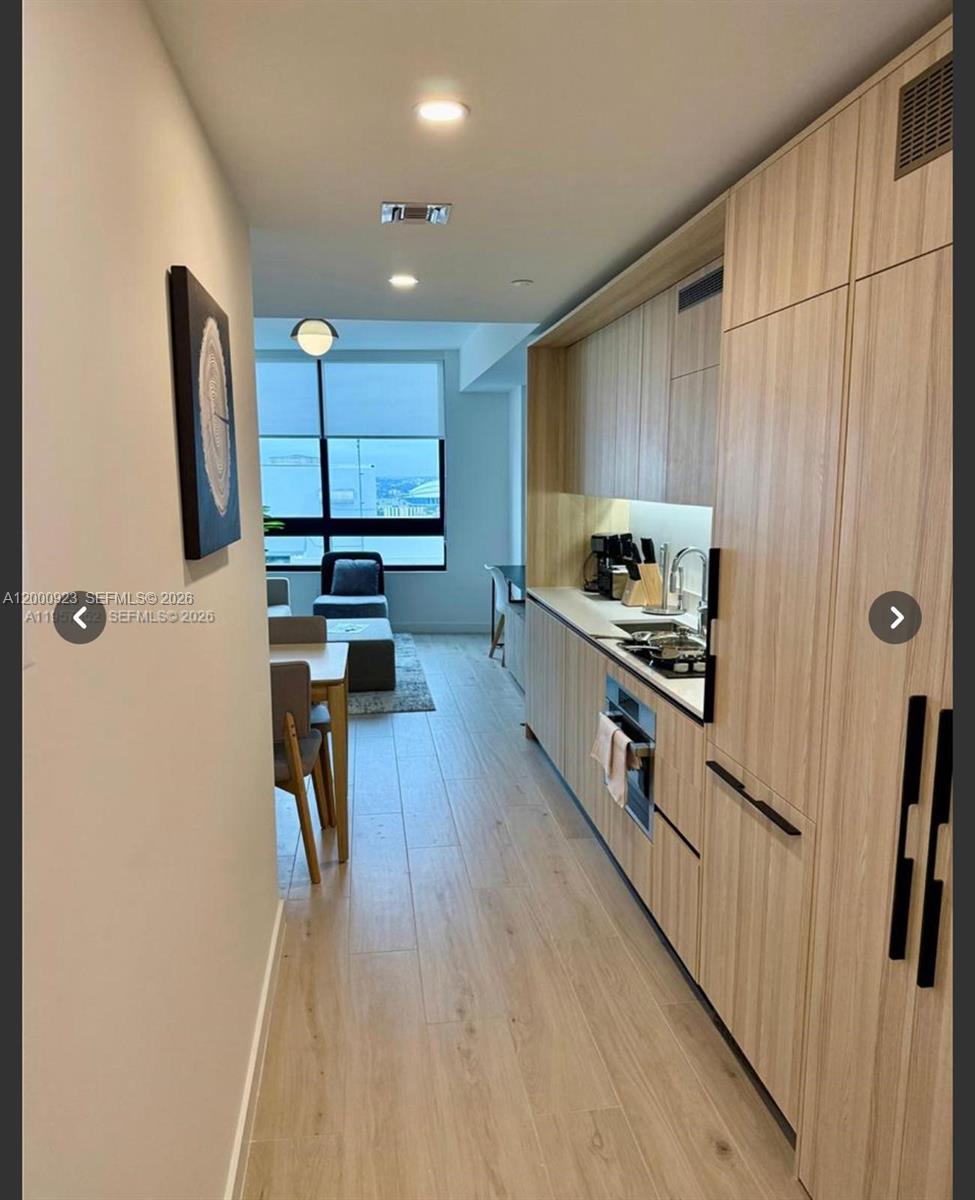 A narrow kitchen with light wood cabinetry leads into a dining area and living space — 225 N Miami Ave # 212, Miami FL 33128, MIAMI, FL