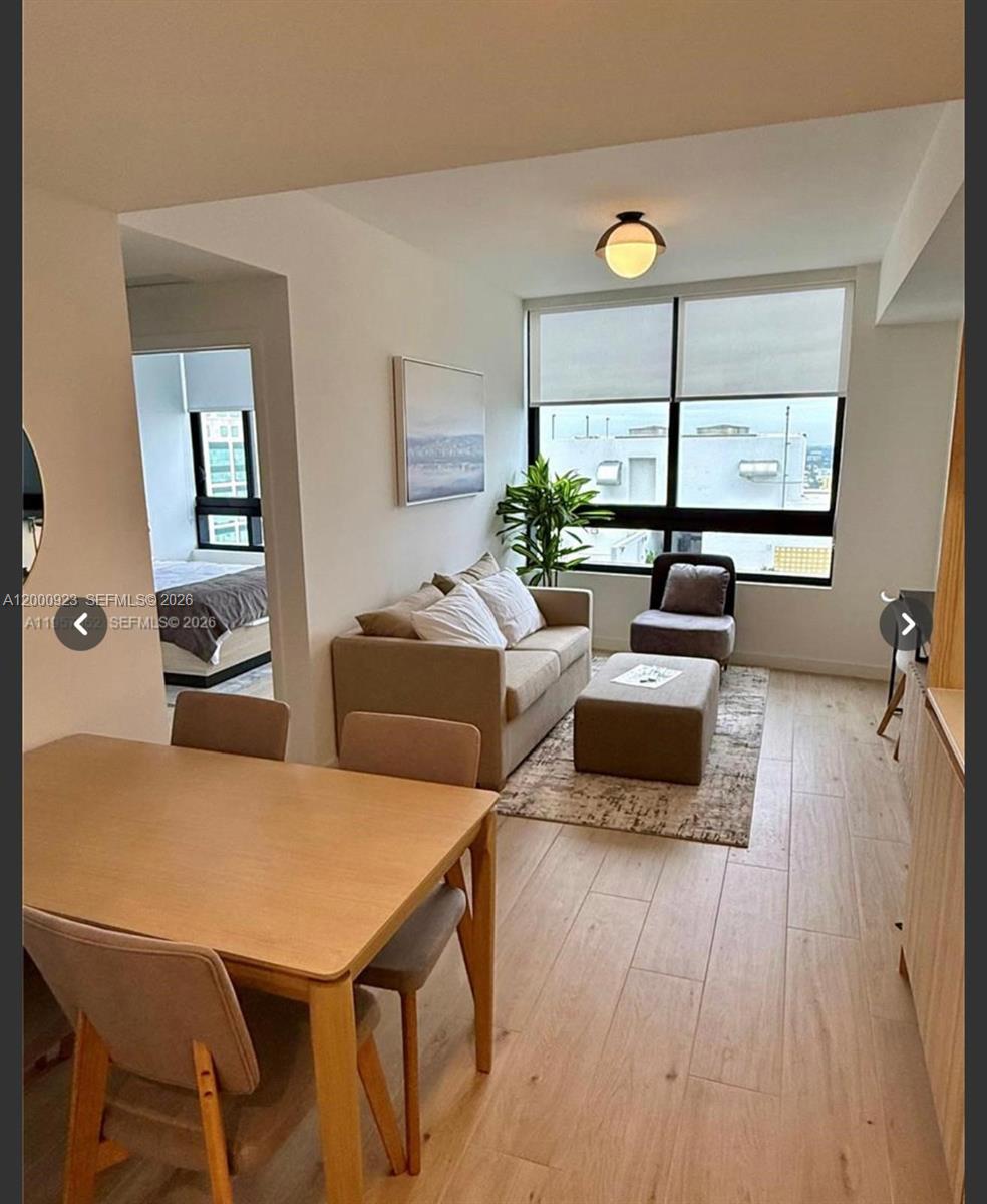 A living room and dining area with light wood flooring, neutral furniture, and large windows — 225 N Miami Ave # 212, Miami FL 33128, MIAMI, FL