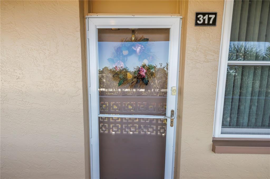 A white storm door with a decorative wreath is installed on a tan stucco exterior — 5095 BAY STREET NE UNIT 317, ST PETERSBURG, FL