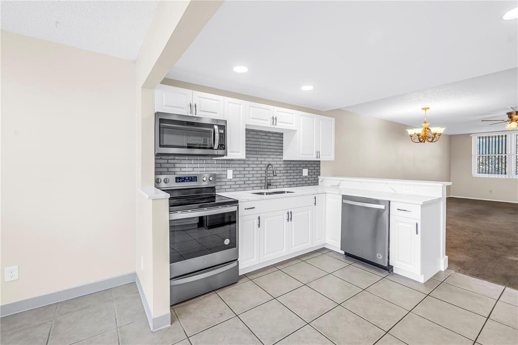 A kitchen features white cabinets, stainless steel appliances, a gray tile backsplash, and tile flooring — 5095 BAY STREET NE UNIT 317, ST PETERSBURG, FL