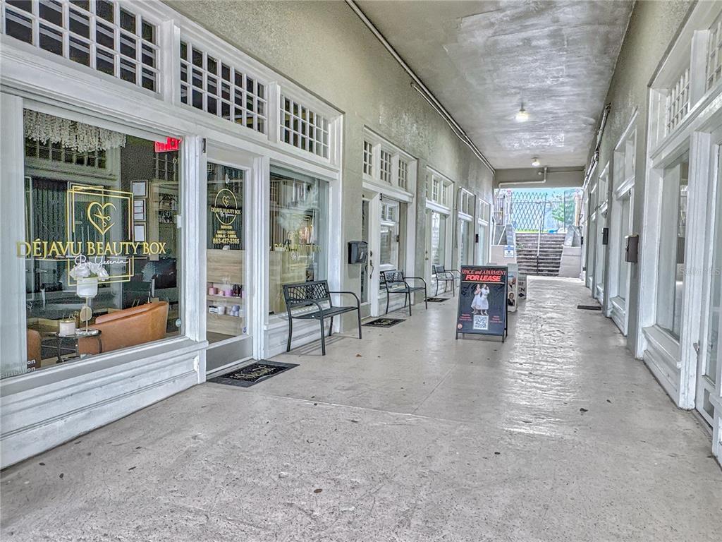 An outdoor covered walkway features storefronts with large windows and benches along a concrete path — 35 N 6TH STREET UNIT 1, HAINES CITY, FL