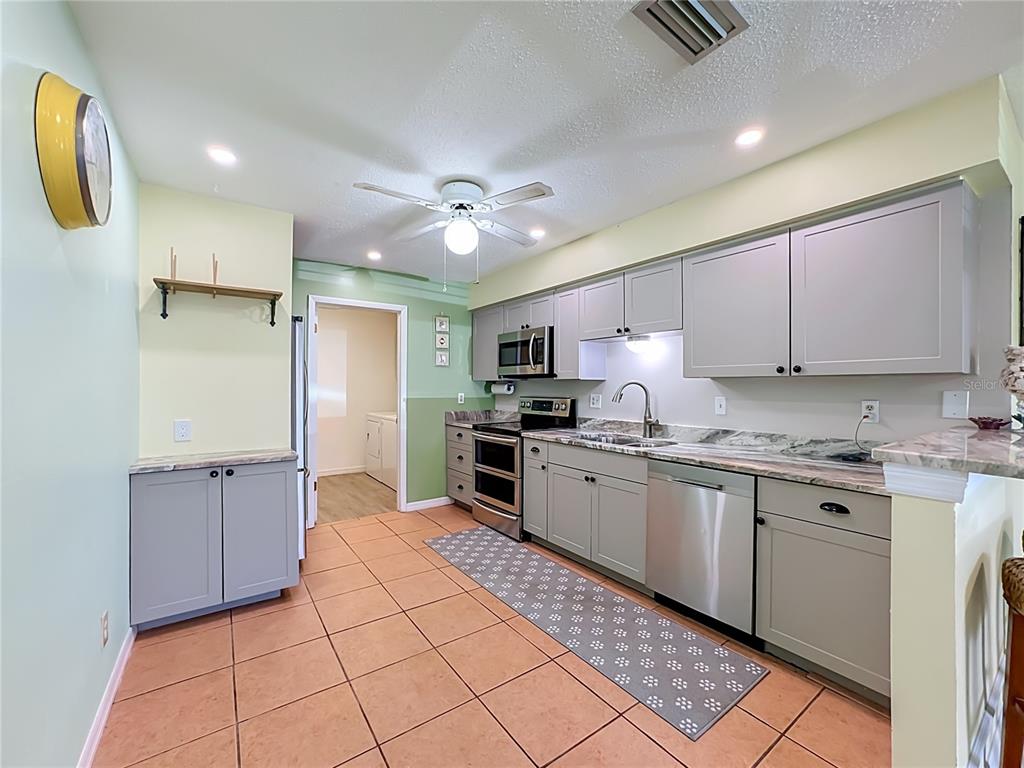 A kitchen features grey cabinets, stainless steel appliances, light countertops, and terracotta-colored floor tiles — 4190 66TH STREET CIRCLE W UNIT O, BRADENTON, FL
