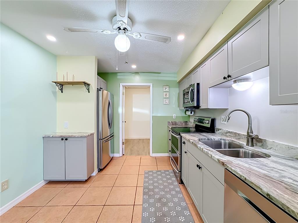 A kitchen features light green walls, grey cabinets, stainless steel appliances, and tiled flooring — 4190 66TH STREET CIRCLE W UNIT O, BRADENTON, FL