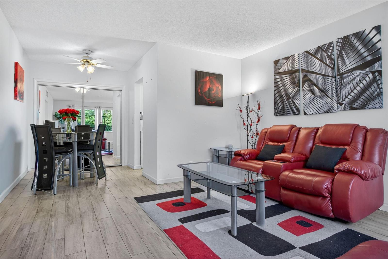 A living room features a red leather sofa, a glass coffee table, and wood-look flooring — 418 S Cypress Road # 110, Pompano Beach FL 33060, POMPANO BEACH, FL