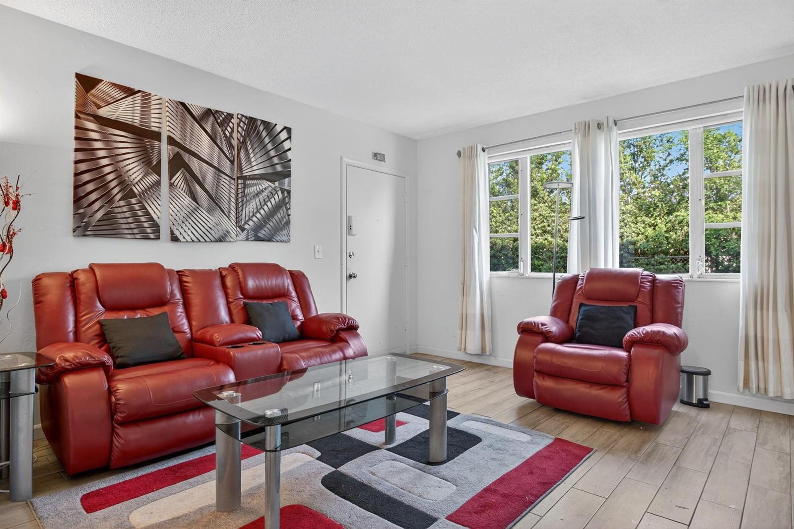 A living room features red leather recliners, a glass coffee table, and a geometric rug — 418 S Cypress Road # 110, Pompano Beach FL 33060, POMPANO BEACH, FL
