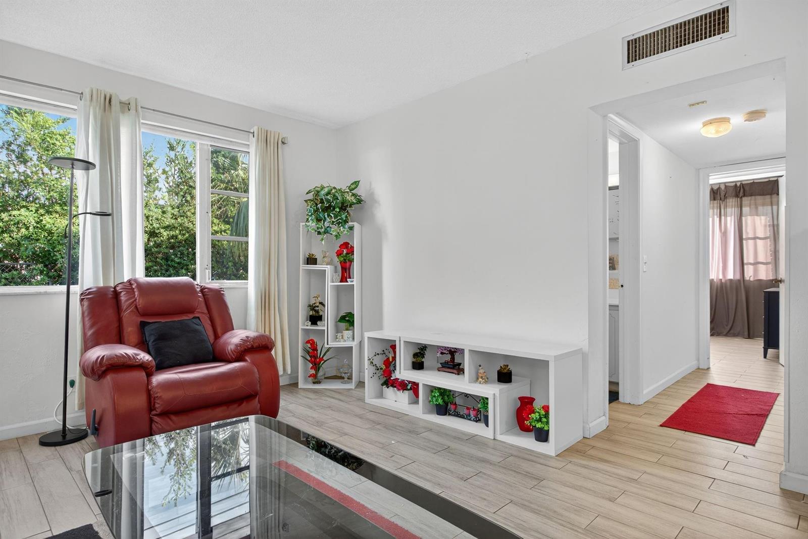 A living room features a red leather recliner, white shelving, and light wood-look tile flooring — 418 S Cypress Road # 110, Pompano Beach FL 33060, POMPANO BEACH, FL